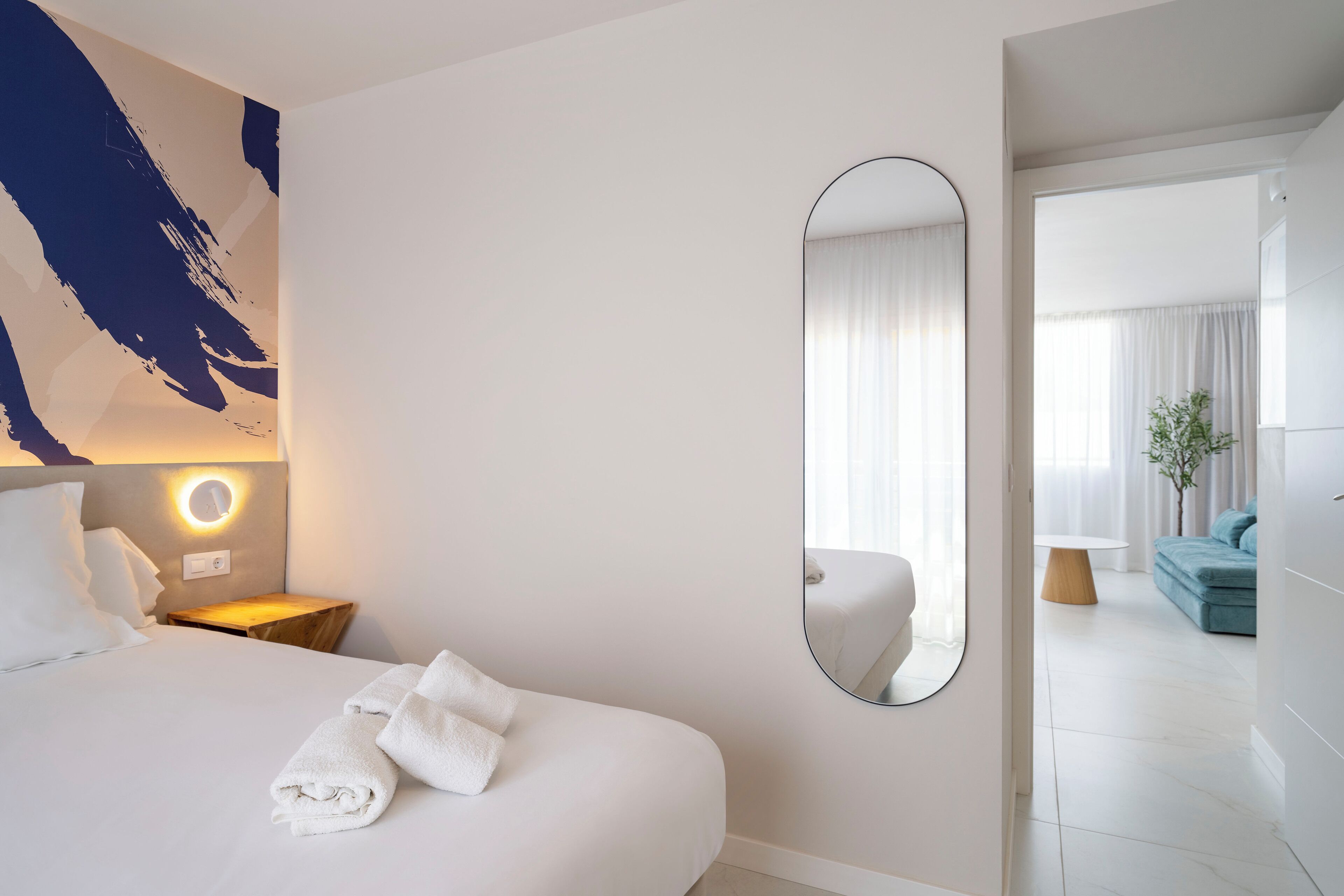 Hotelkamer met een bed, een ronde spiegel, een nachtkastje met lamp en uitzicht op de zithoek.