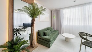 Una sala de estar moderna con un espejo grande, sofá verde, mesa de centro blanca y una zona de comedor con sillas.