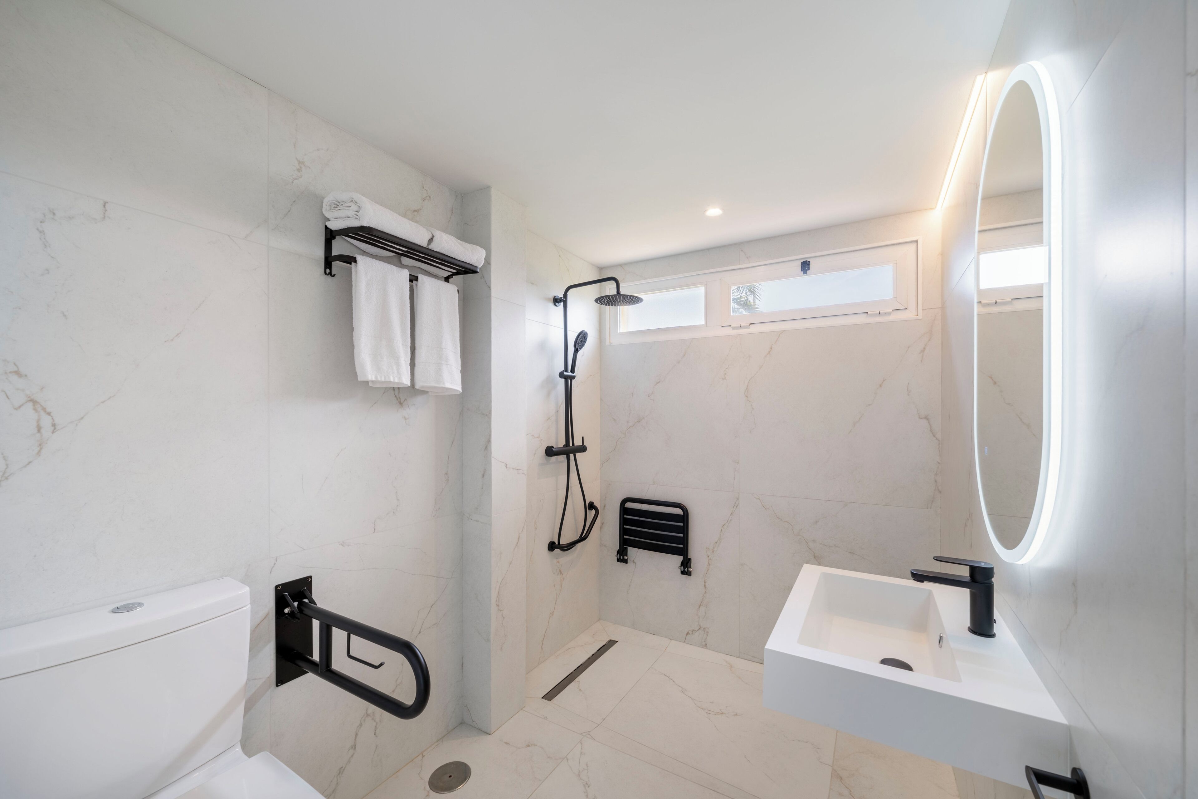 A modern bathroom with a shower, toilet, sink, and a mirror with built-in lighting.