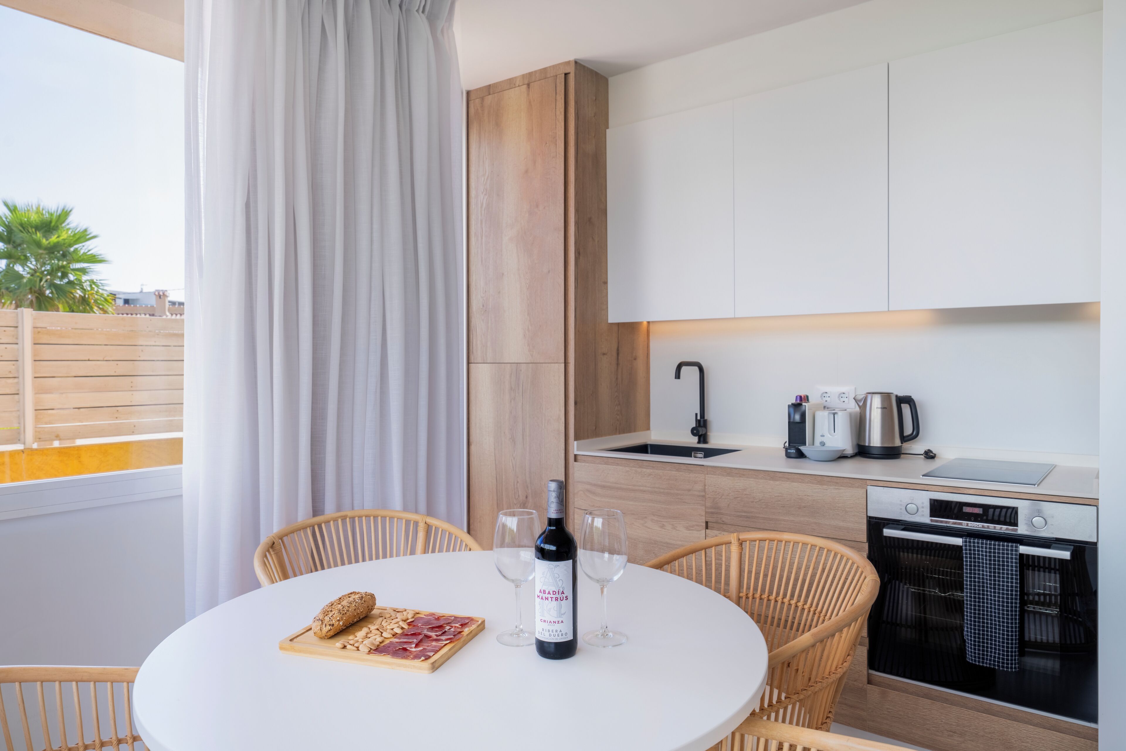 A modern kitchen with a round dining table, two chairs, a bottle of wine, and a cutting board with food.