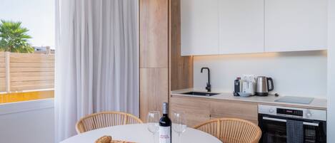 A modern kitchen with a round dining table, two chairs, a bottle of wine, and a cutting board with food.