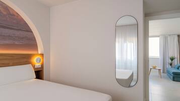 Habitación de hotel con una cama grande, un espejo redondo y vista al área de estar a través de una puerta abierta.