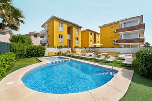 A swimming pool surrounded by lounge chairs and a yellow building with balconies.