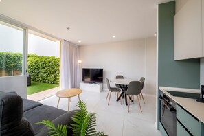 A modern living room with a sofa, a dining table with chairs, a TV, and a kitchen area with cabinets.
