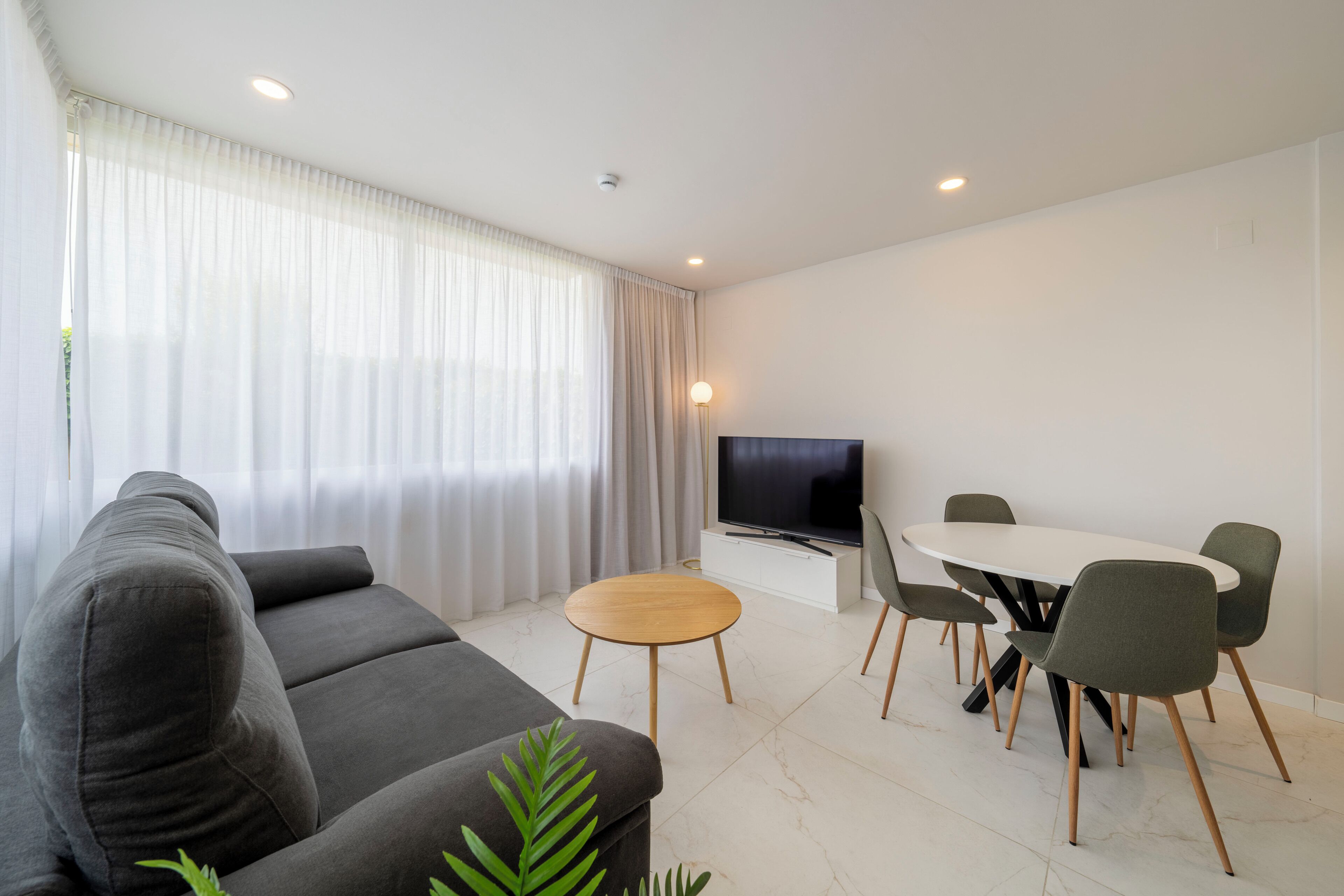 A modern living room with a sofa, a TV, a dining table with chairs, and a small round table.