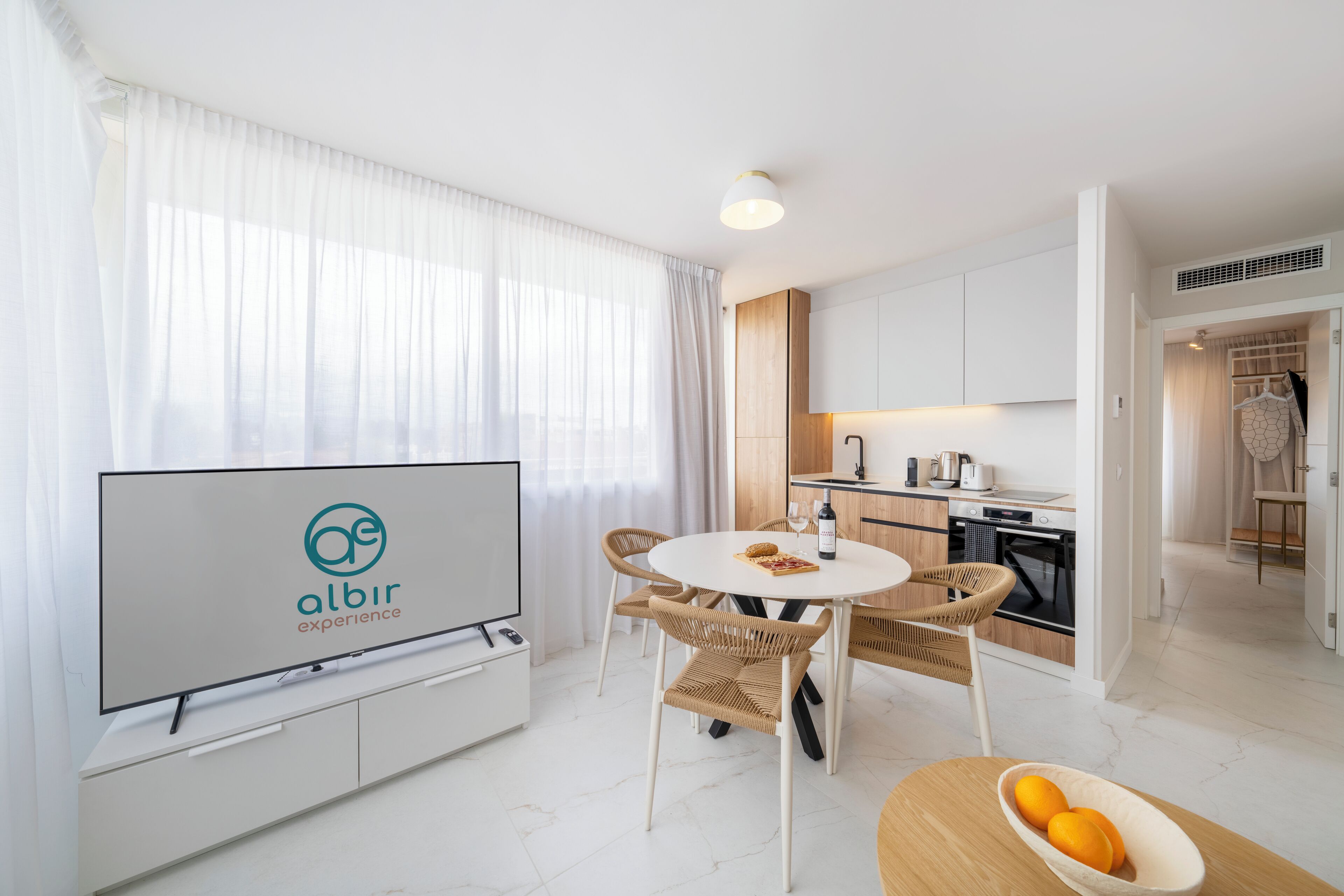 Ein modernes Hotelzimmer mit Essbereich, Küchenzeile und einem Fernseher, der das Logo "albir experience" zeigt.