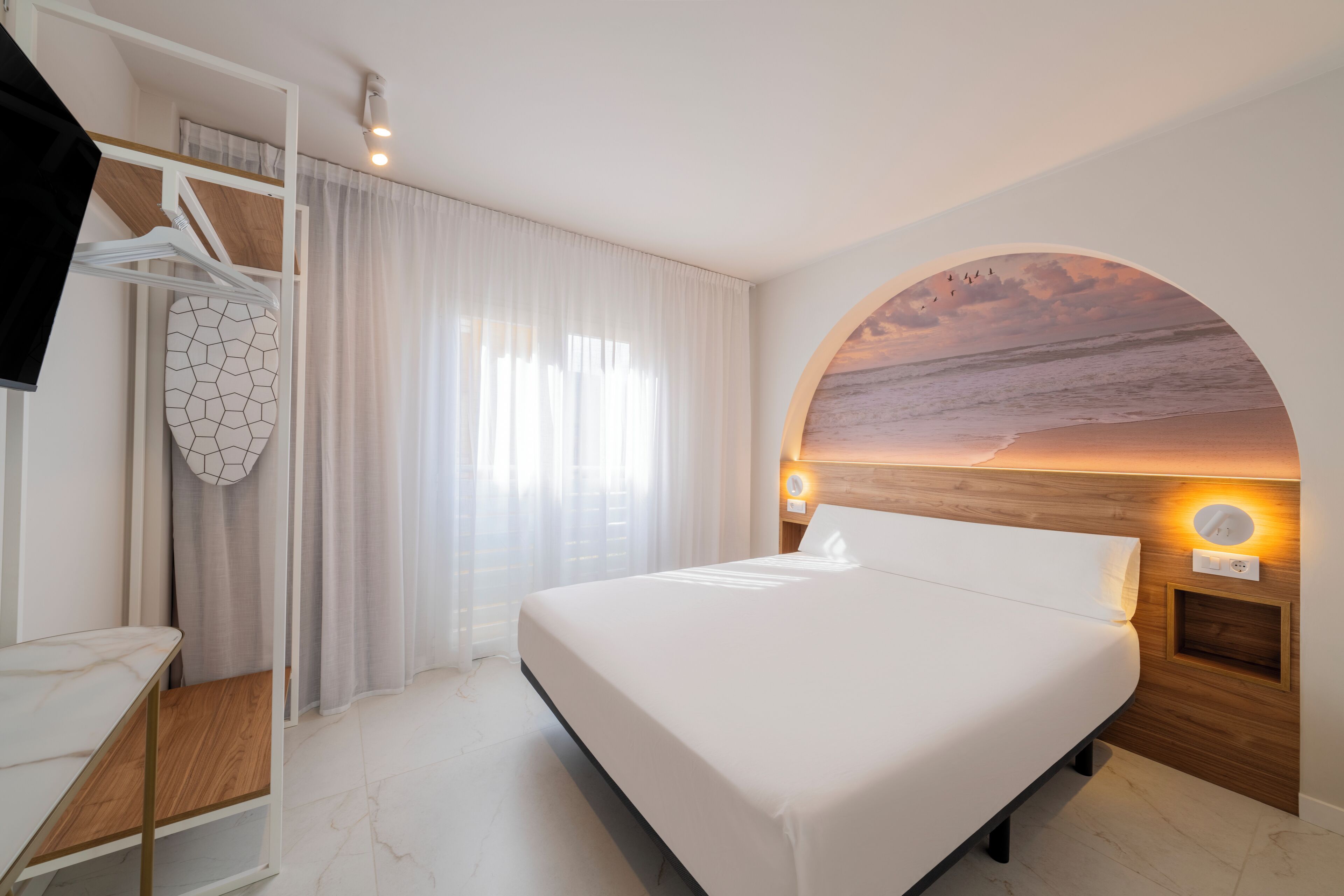 Une chambre d’hôtel moderne dotée d’un grand lit, d’une télévision, d’un bureau et offrant une vue sur la plage grâce à une fenêtre circulaire.