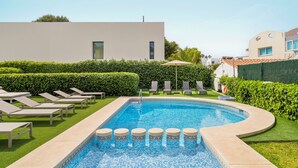 Una piscina con sillones de descanso y un edificio moderno al fondo.