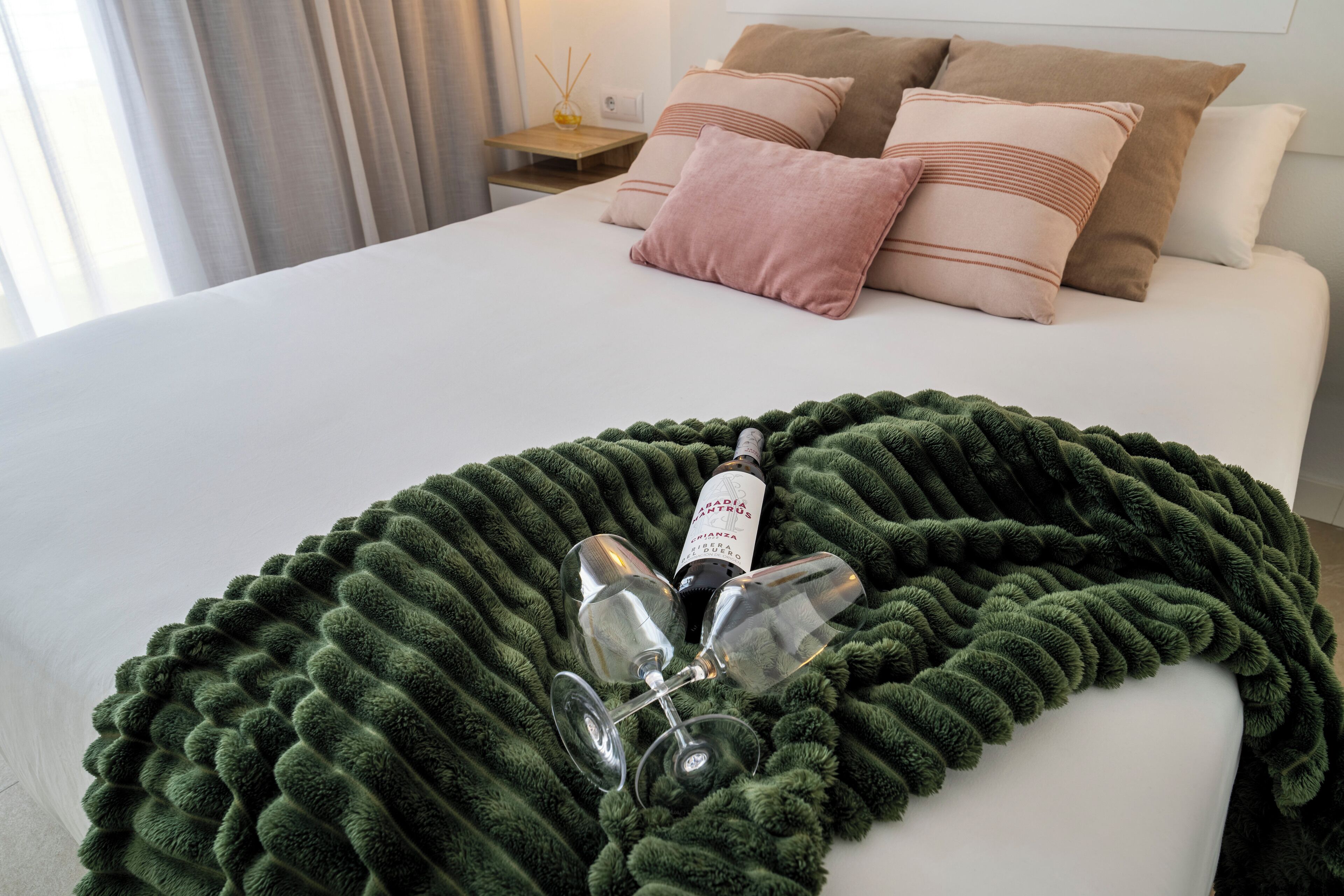 Ein ordentlich bezogenes Bett mit einer grünen Decke, zwei Weingläsern und einer Weinflasche auf dem Bett.