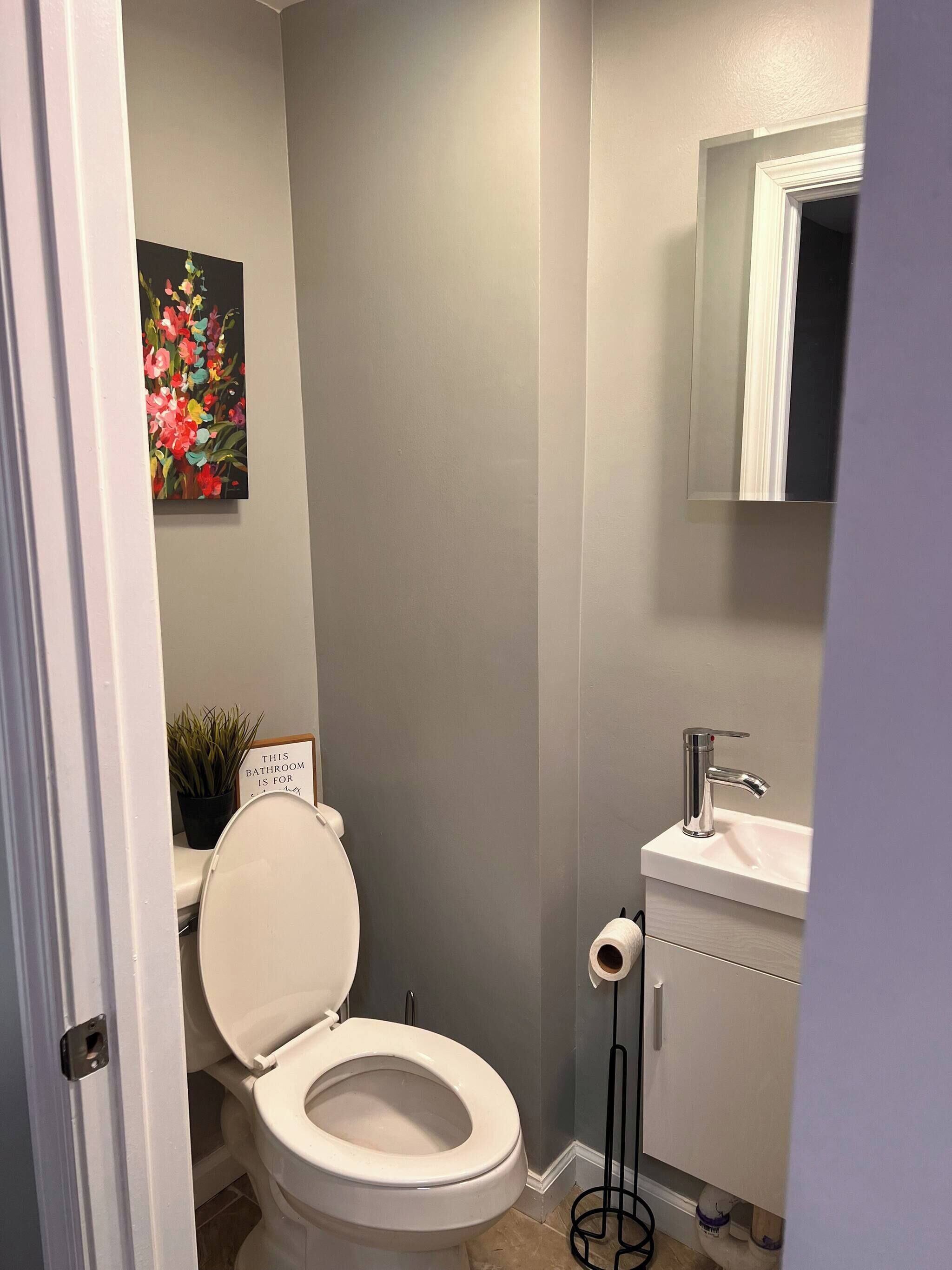 A bathroom with a toilet, sink, and a framed sign on the wall.