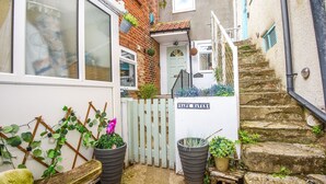 Une ruelle étroite avec une porte blanche portant l’inscription « REFUGE », un banc en bois et des plantes en pot.