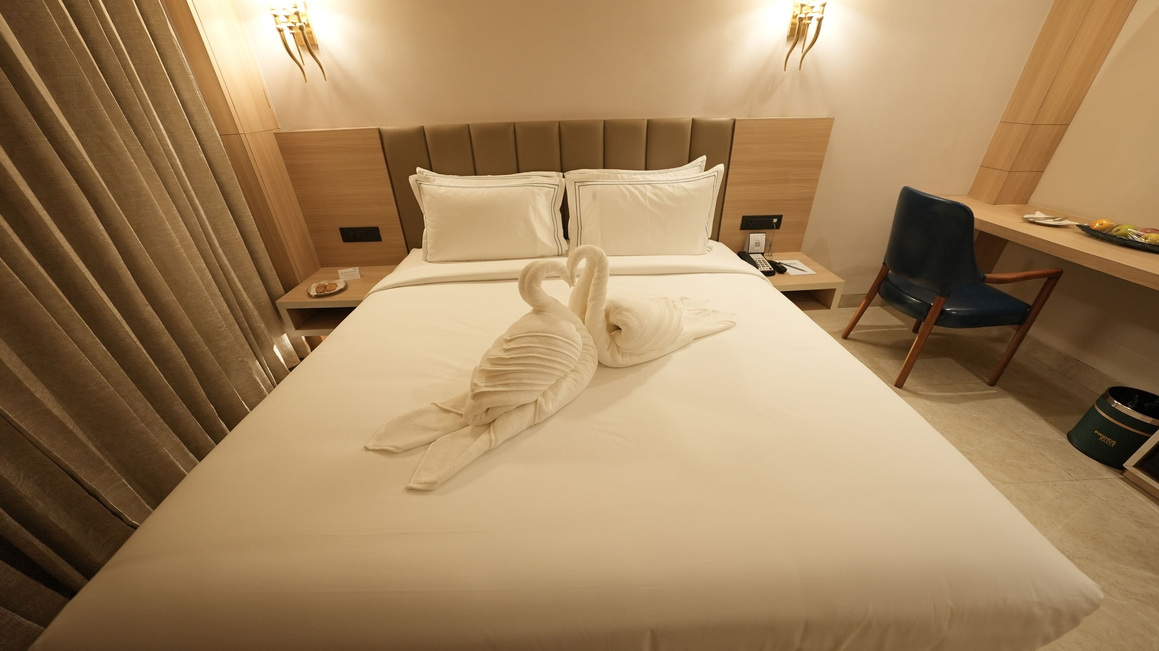 Een hotelkamer met een net opgemaakt bed, een bureau met stoel en een nachtkastje met telefoon en lamp.