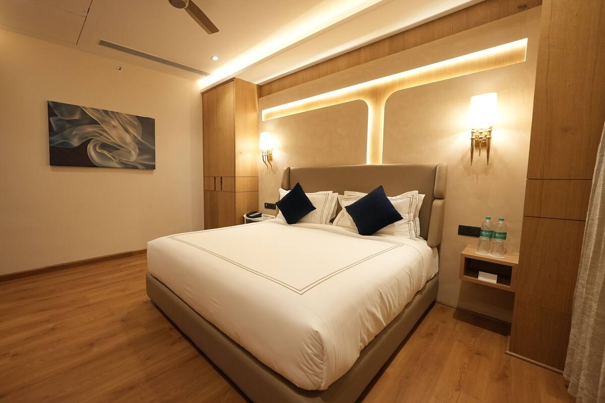 A modern hotel room with a large bed, wooden headboard, and a painting on the wall.