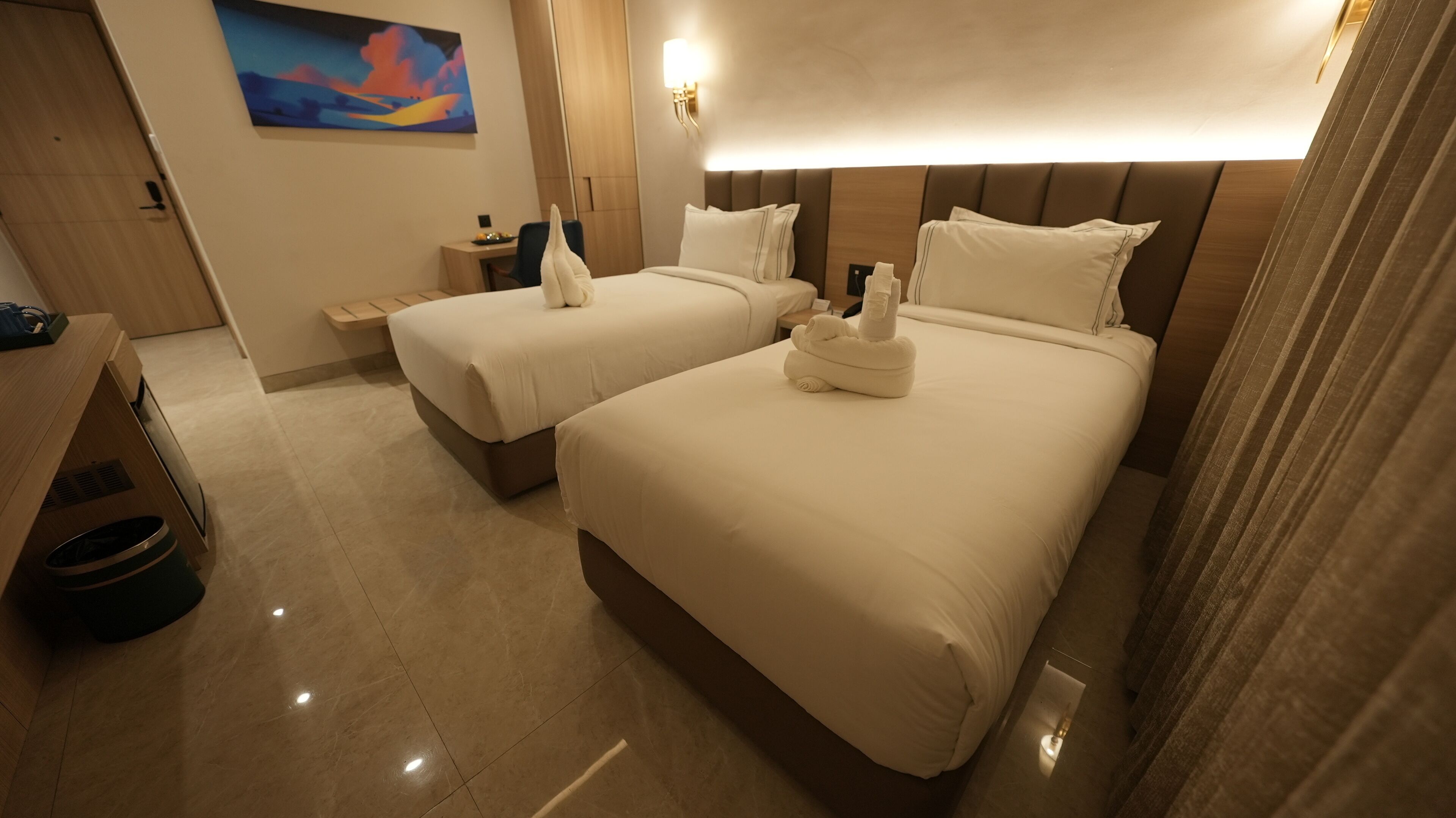 Una habitación de hotel con dos camas, un escritorio, una silla, un cuadro y una mesita de noche.