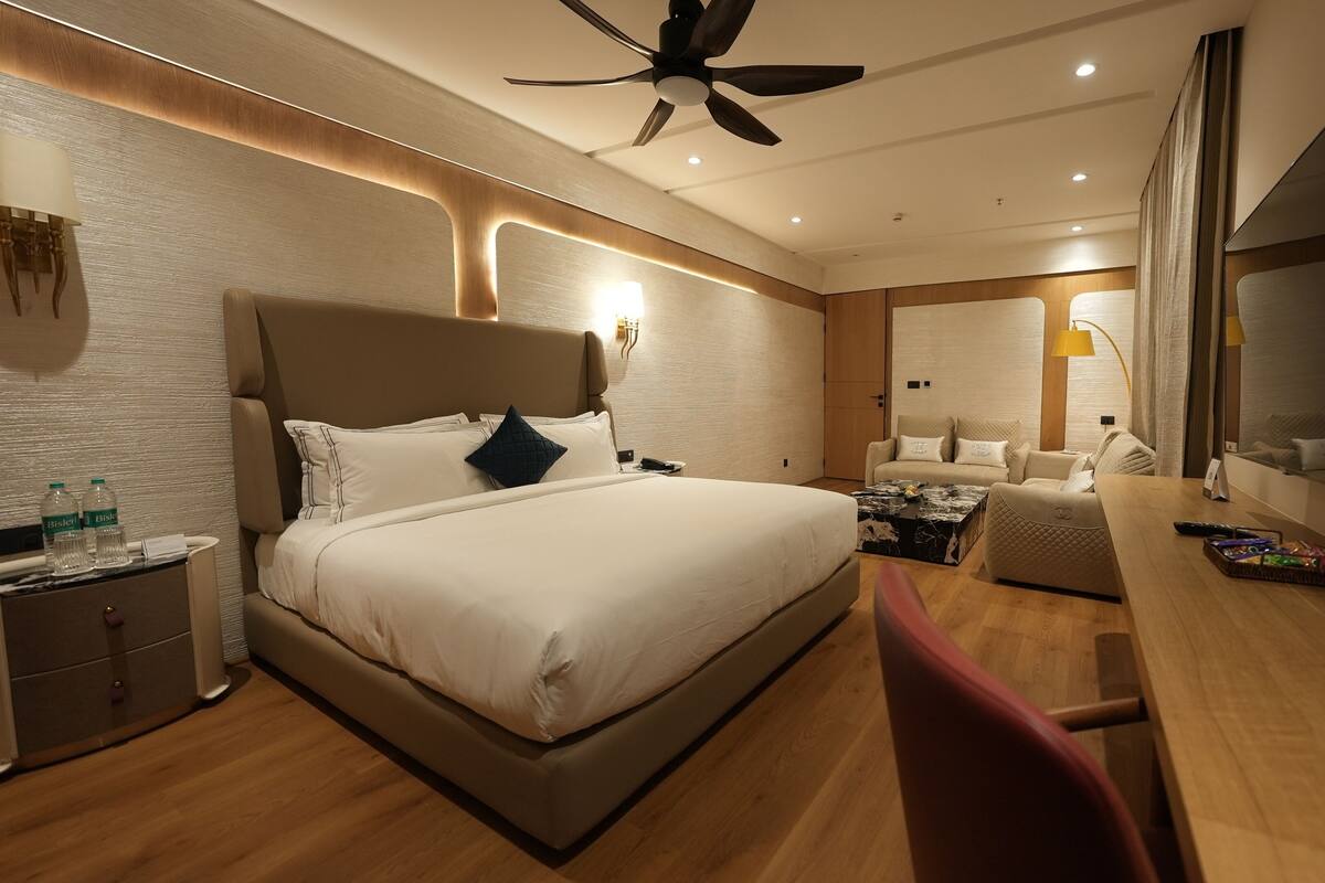 A modern hotel room with a large bed, a desk, a chair, a ceiling fan, and a large mirror.