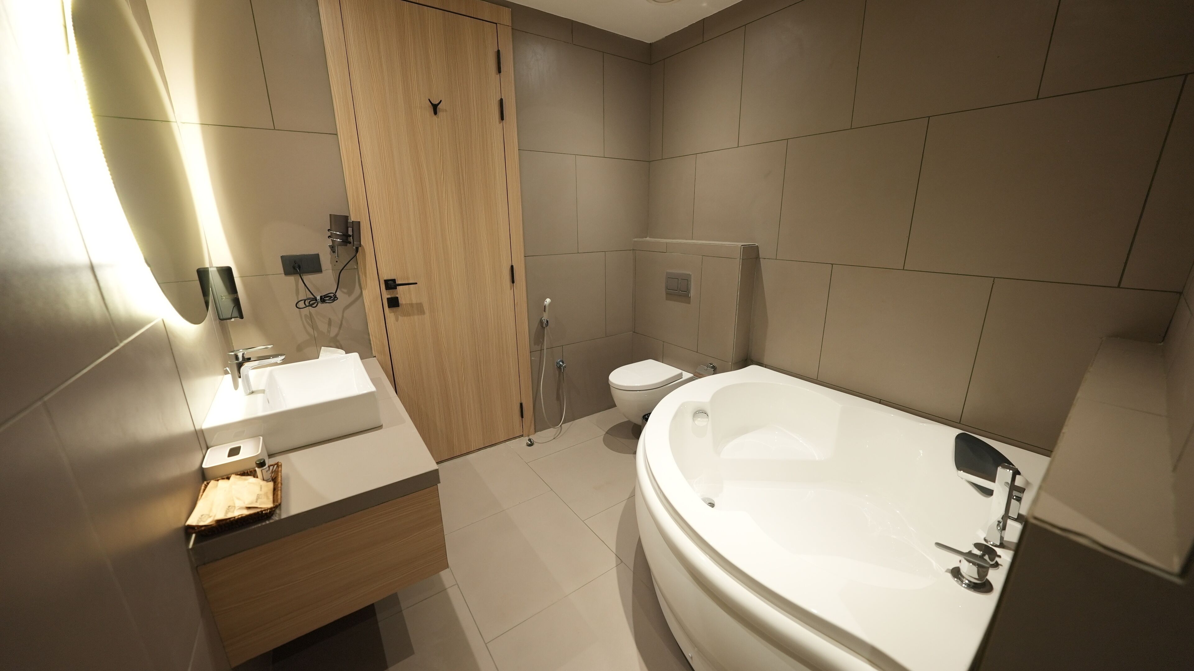 Een moderne badkamer met een houten deur, een witte wasbak, een toilet en een ruime badkuip.