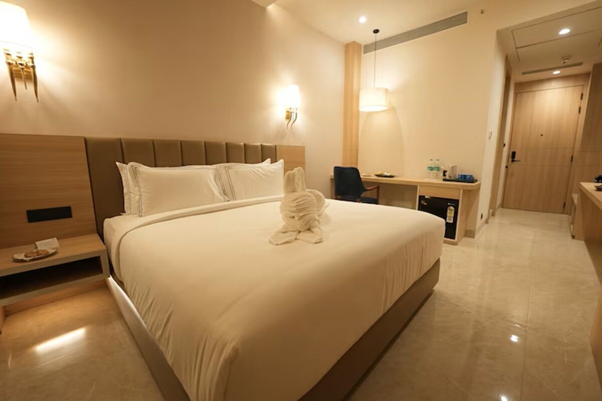 A hotel room with a large bed, bedside table, lamp, desk, and a mirror.