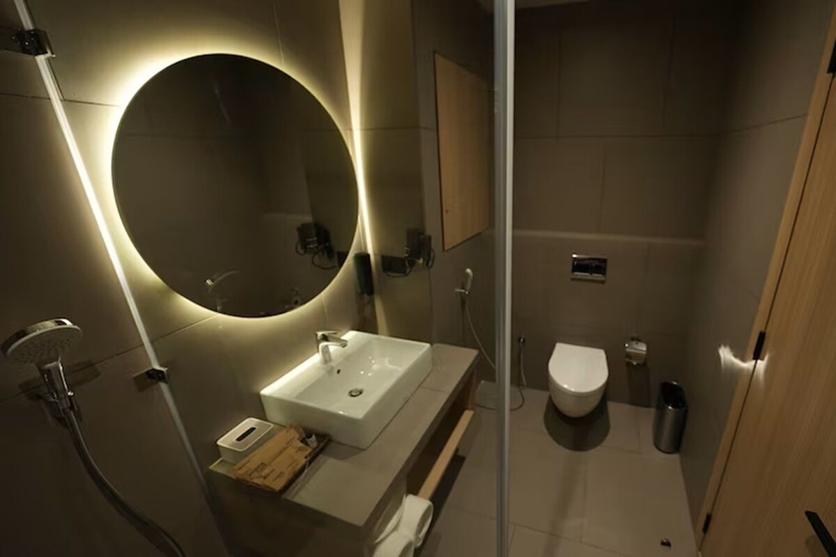 A modern bathroom with a round mirror, a sink, a toilet, and a shower area.