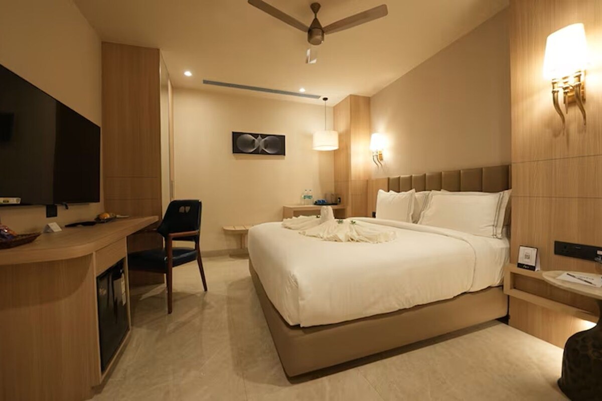 A hotel room with a bed, desk, chair, and a television.