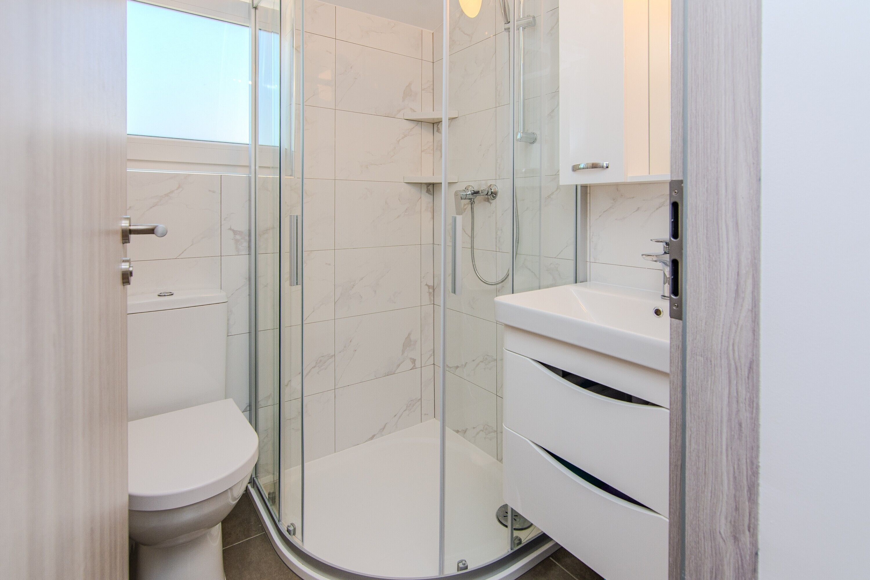 Een moderne badkamer met een douchecabine van glas, een wit toilet en een wastafel met spiegel.