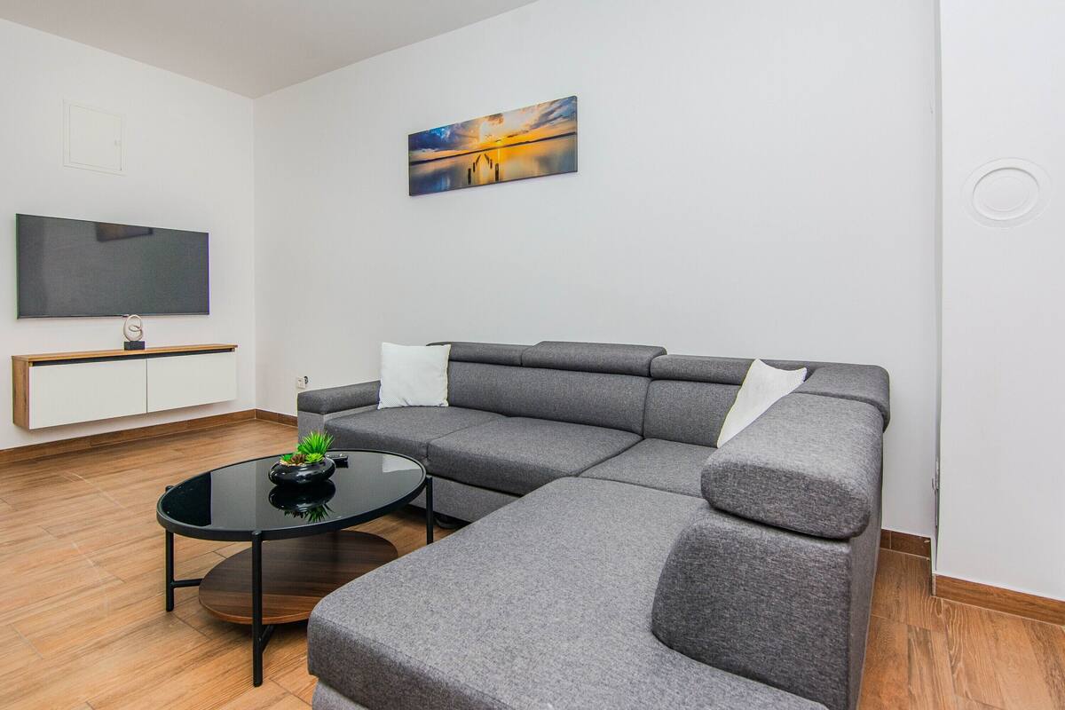 A modern living room with a sectional sofa, a flat-screen TV, a coffee table, and a painting on the wall.
