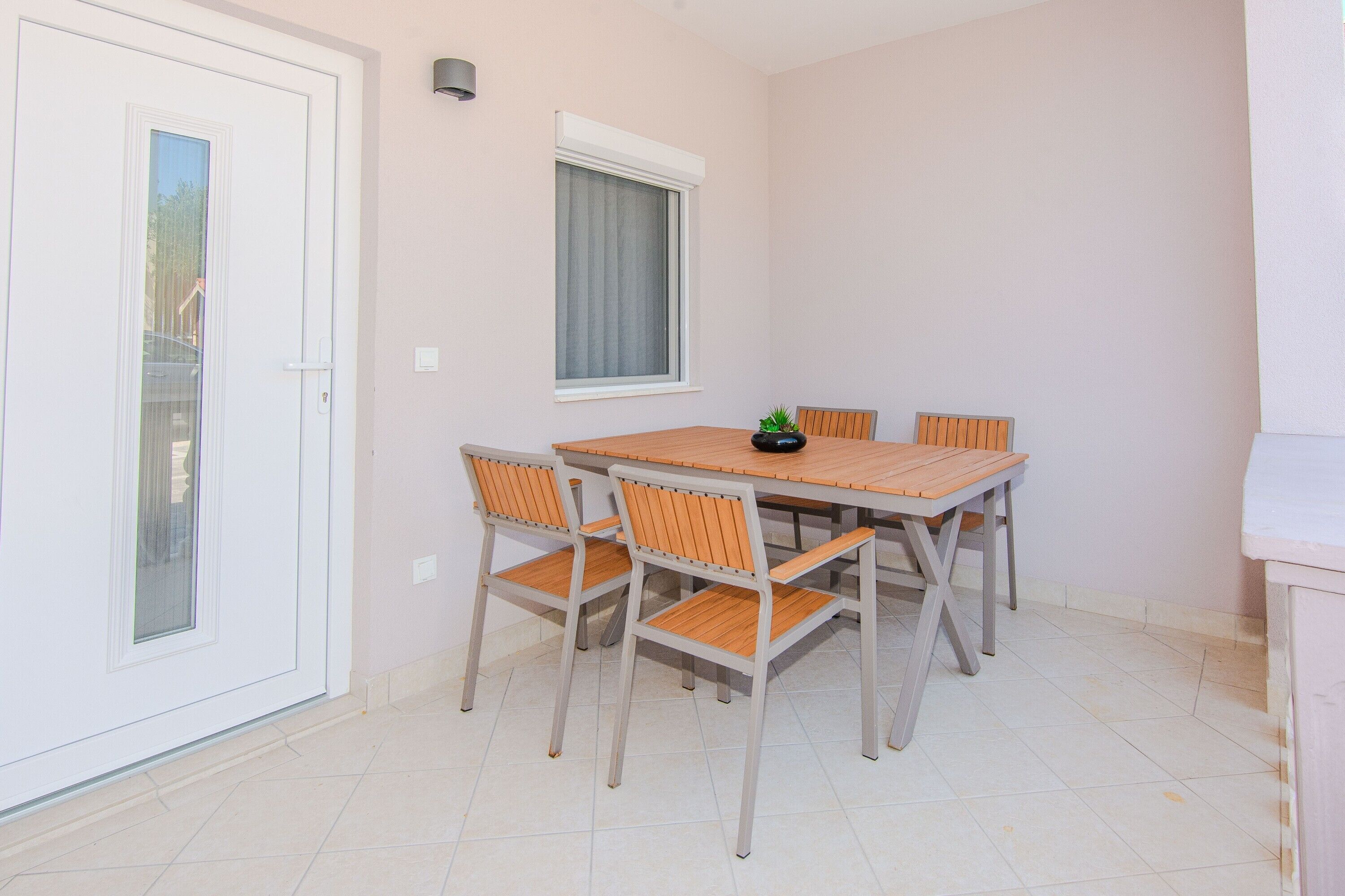 A dining area with a wooden table and four chairs, a potted plant, and a window with curtains.