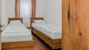 A room with two wooden beds, white bedding, a window with curtains, and a wooden floor. - Apartments Mucaj (Vir)