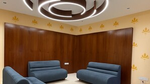 A modern waiting area with two blue sofas, wooden panel walls, and a circular ceiling light fixture. - HOTEL HILL PARK (Indore)