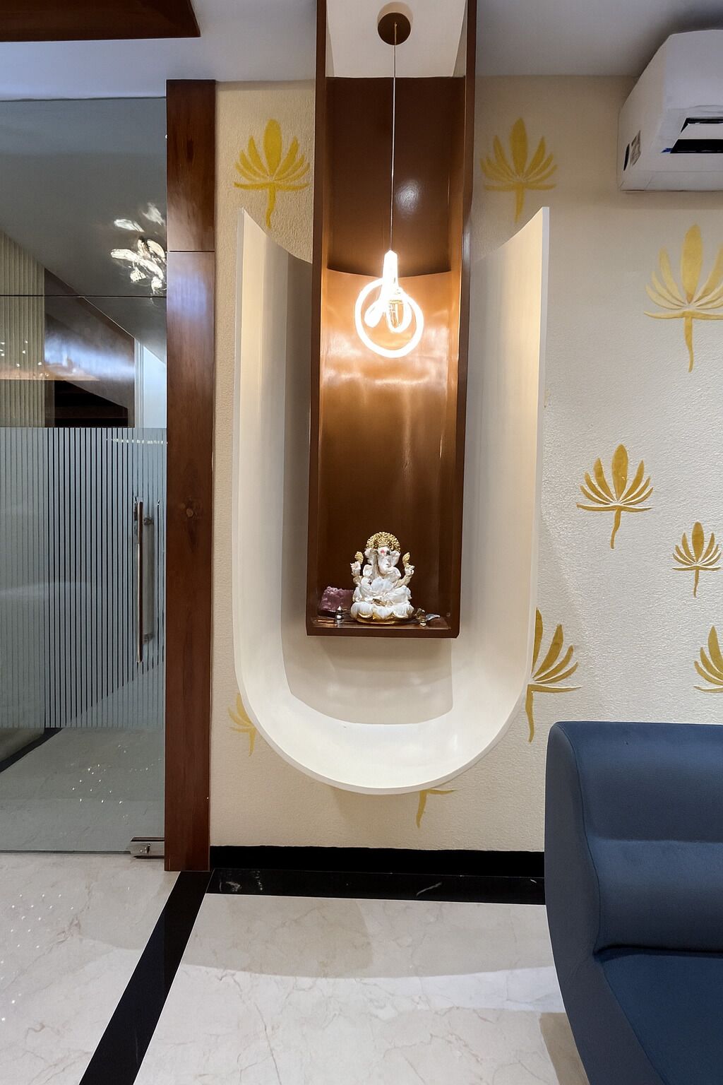 A modern interior with a recessed wall shelf holding a statue, a hanging light fixture, and a wall with a lotus pattern.