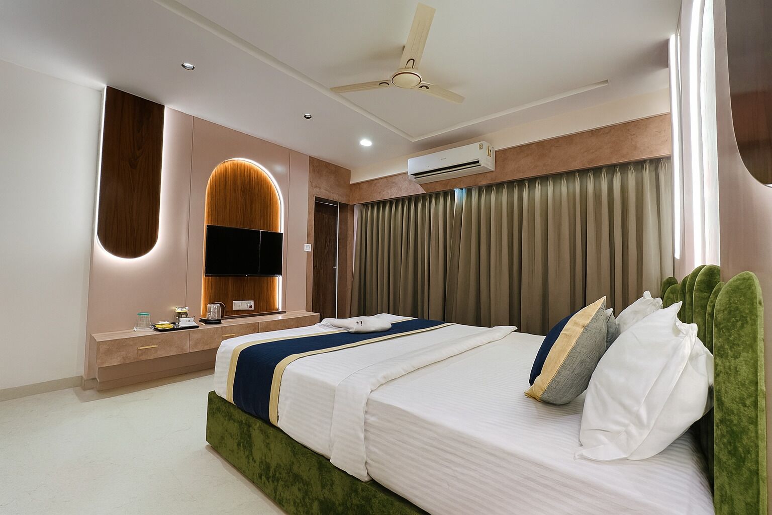A modern hotel room with a large bed, a vanity with a mirror, a ceiling fan, and an air conditioning unit.