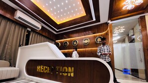 A reception area with a wooden reception desk, a clock, and a ceiling with recessed lighting. - HOTEL HILL PARK (Indore)
