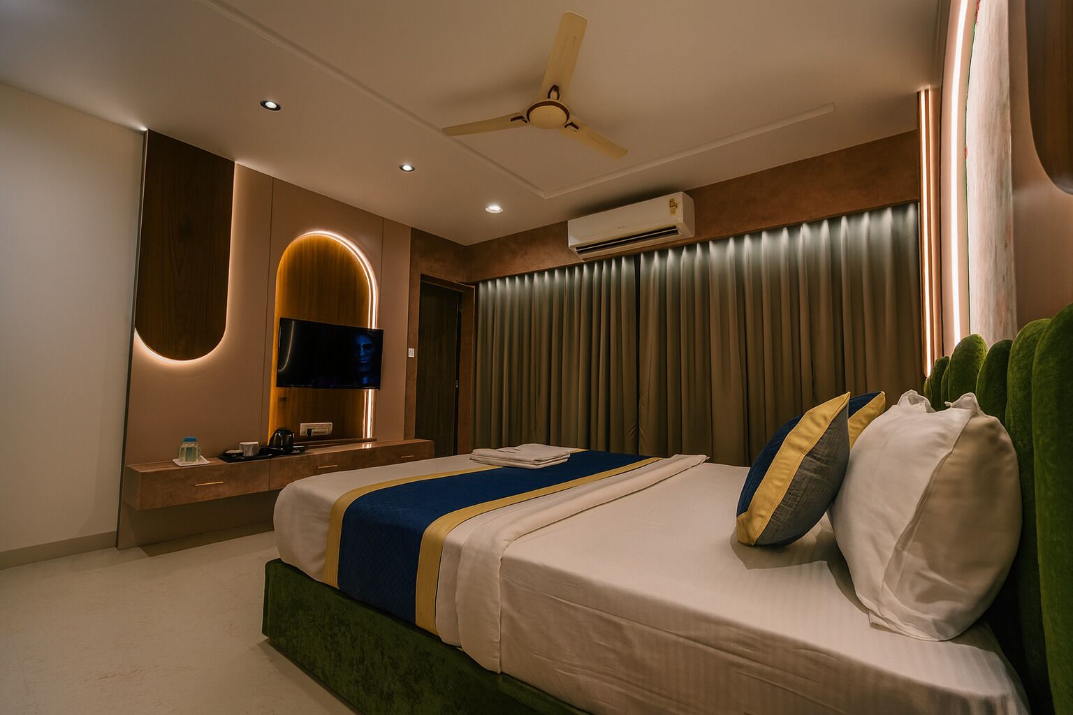 A modern hotel room with a bed, a vanity with a mirror, an air conditioning unit, and a ceiling fan.