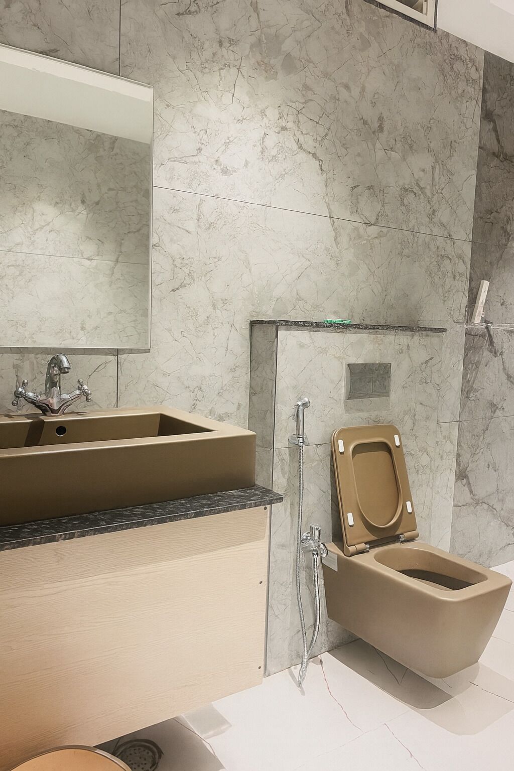 Een badkamer met een marmeren wand, een beige wastafel, een spiegel, een toilet en een douche.