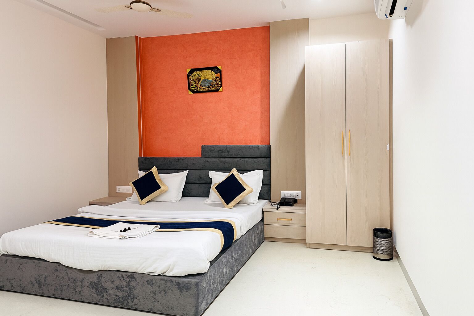 Una habitación de hotel moderna con cama, mesita de noche, armario y un elemento decorativo en la pared.