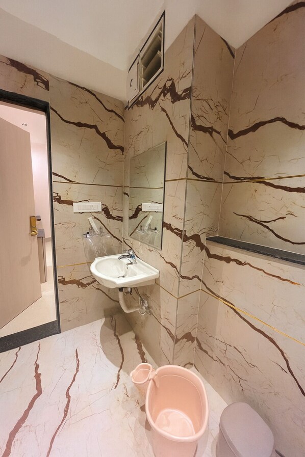 A bathroom with a marble wall, a sink, a mirror, and a toilet.