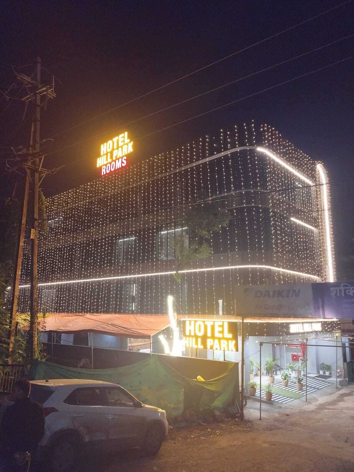 Un hôtel avec une enseigne indiquant « CHAMBRES DE L’HÔTEL HILL PARK » et une grande structure illuminée.
