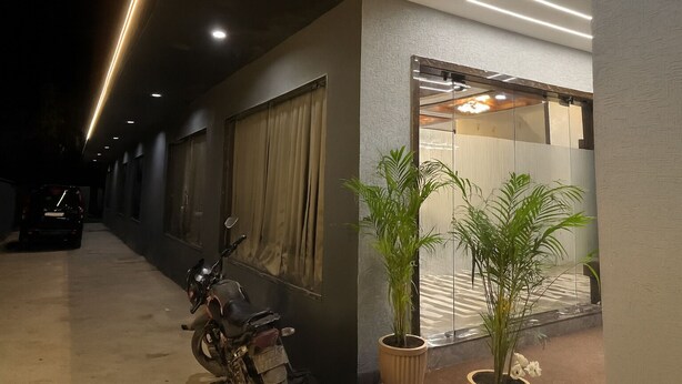 A hallway with a parked motorcycle, a potted plant, and a reflective glass door leading to a room. - HOTEL HILL PARK (Indore)