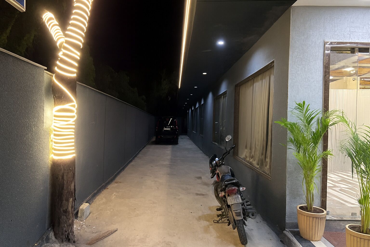 A narrow corridor with a motorcycle parked on the right, a car in the distance, and a decorative light on the left.