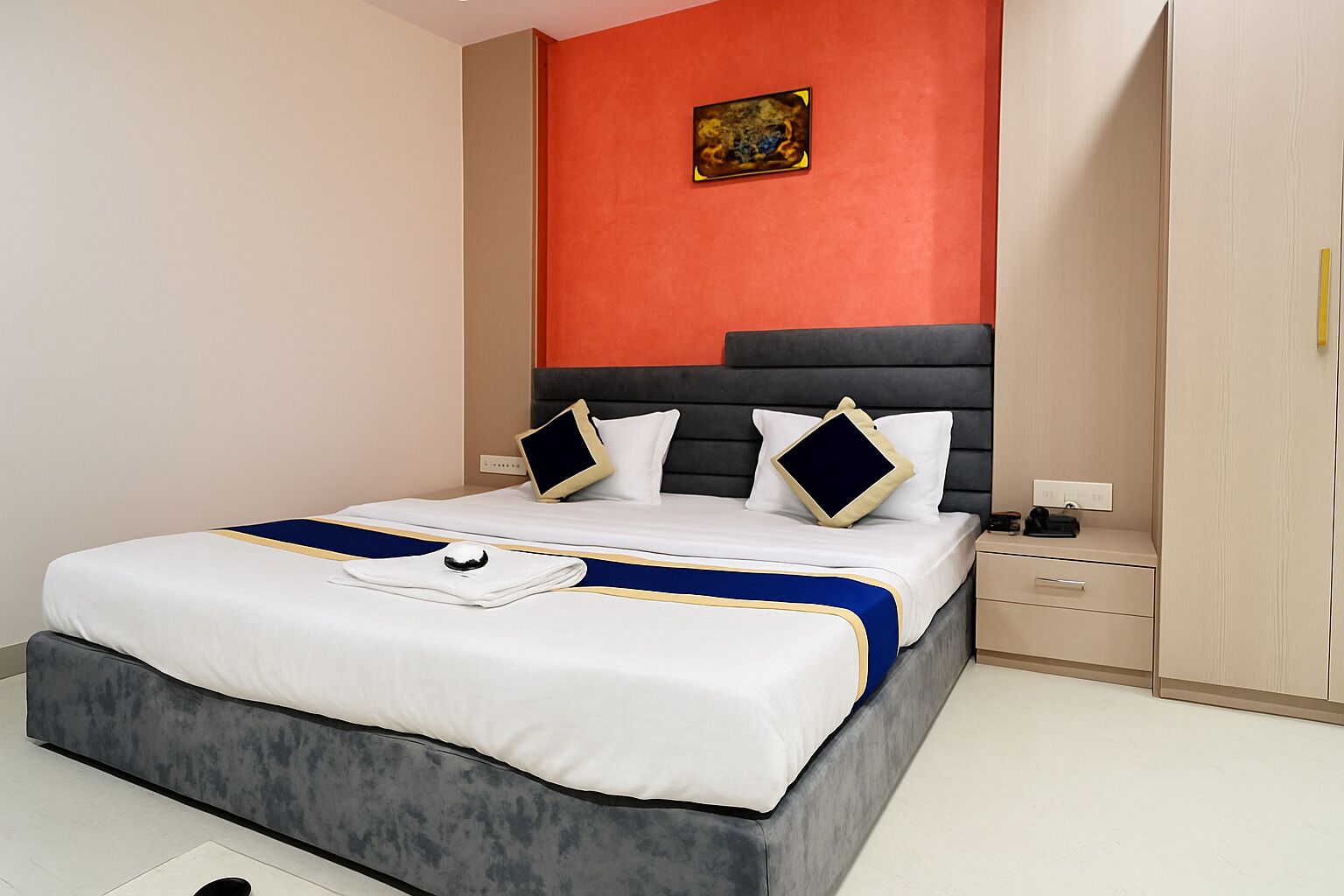 Ein modernes Hotelzimmer mit einem großen Bett, einem Nachttisch, einem Kleiderschrank und einem Bild an der Wand.