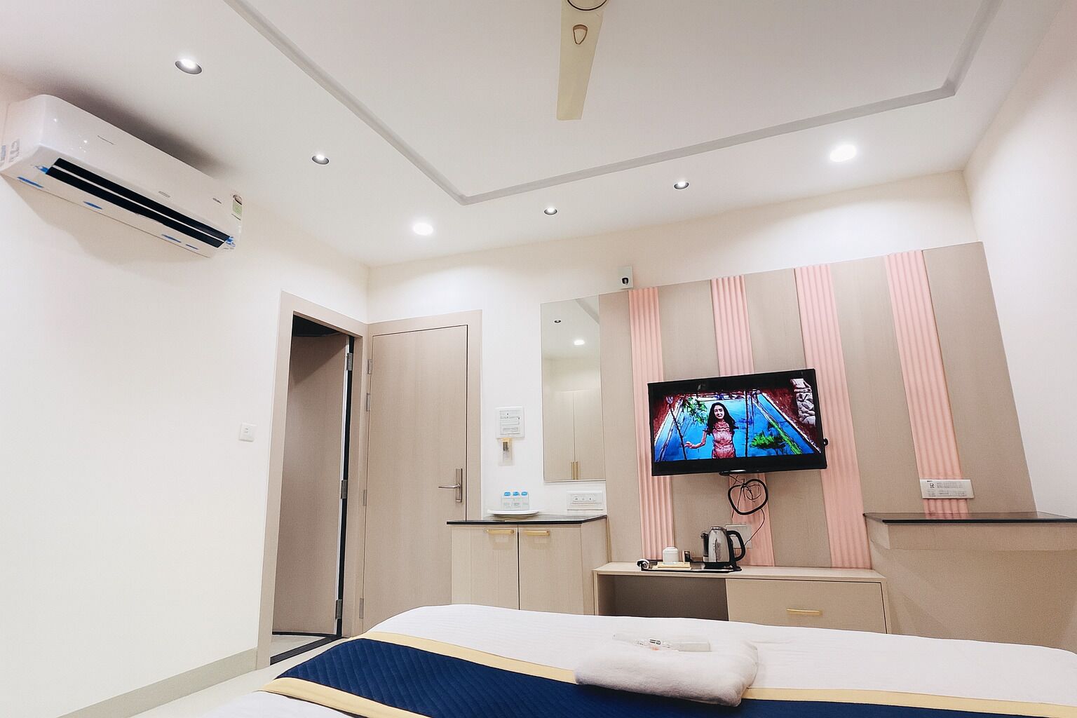 Une chambre d’hôtel comprenant un lit, un téléviseur fixé au mur, une table de chevet, un miroir, un appareil de climatisation et une porte.