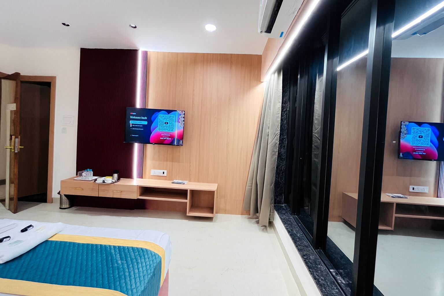 A modern hotel room with a bed, a desk, and two flat-screen TVs mounted on the wall.