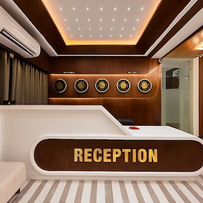 A reception area with a wooden reception desk, a clock, and a ceiling with recessed lighting. - HOTEL HILL PARK (Indore)