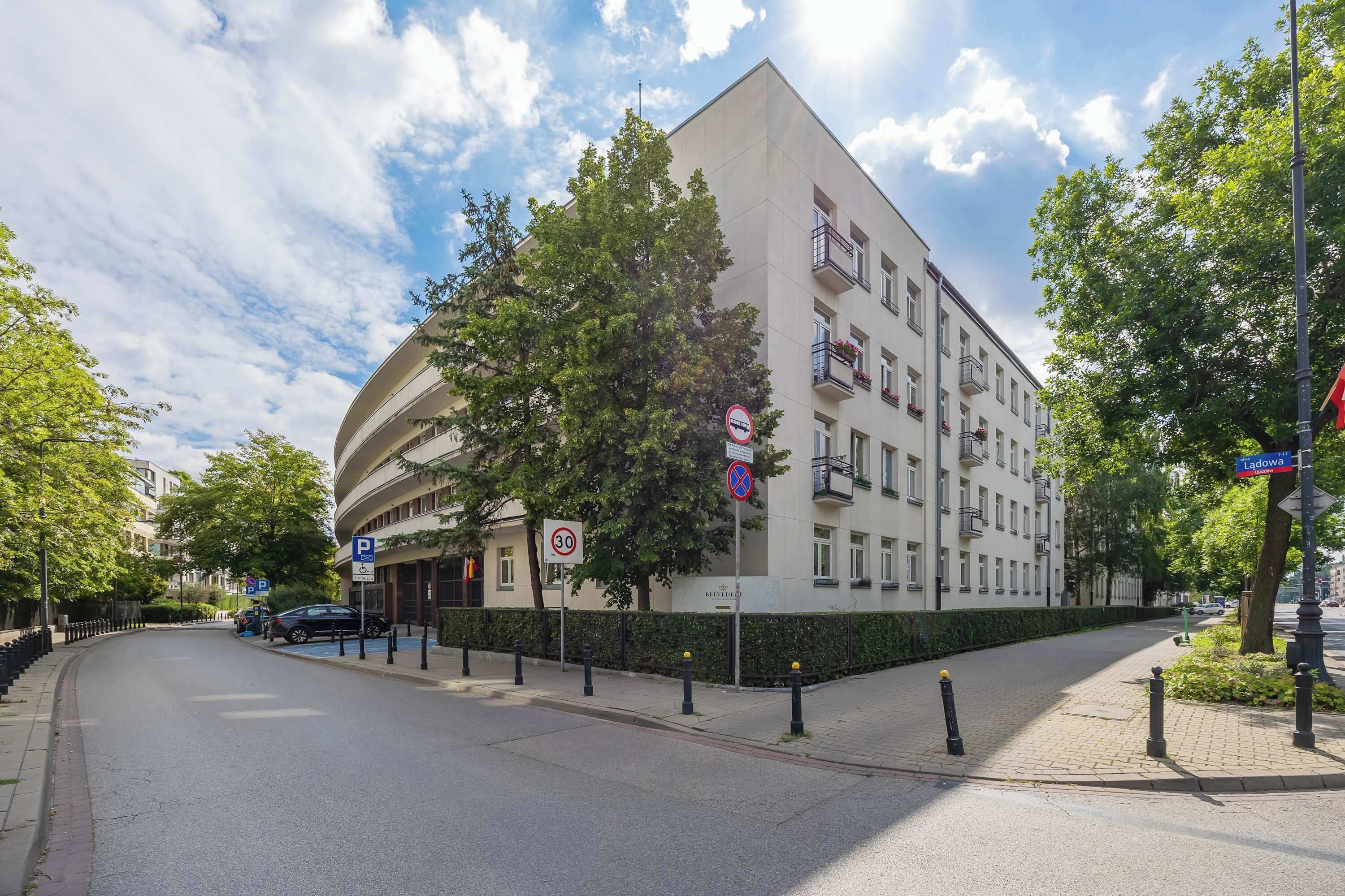 A multi-story building with a curved facade, a no parking sign, and a street with bollards.