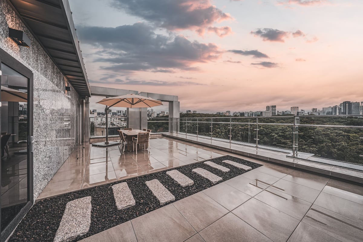 A rooftop terrace with a dining area, a view of the city skyline, and a glass railing.