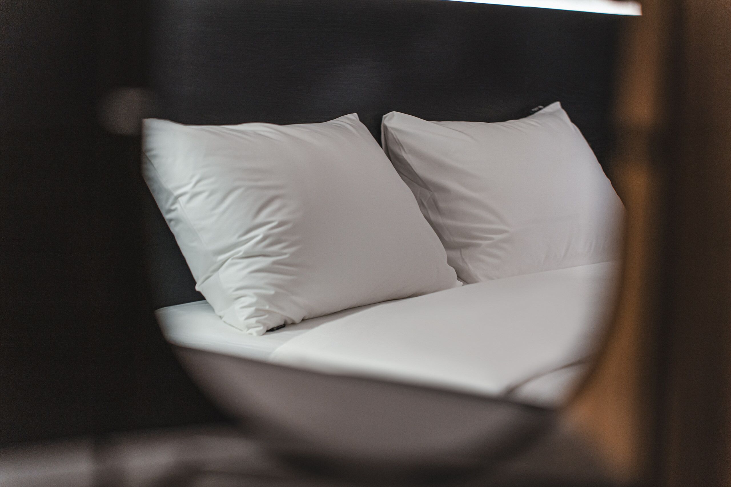 A modern bed with white linens and two pillows in a room with dark walls.