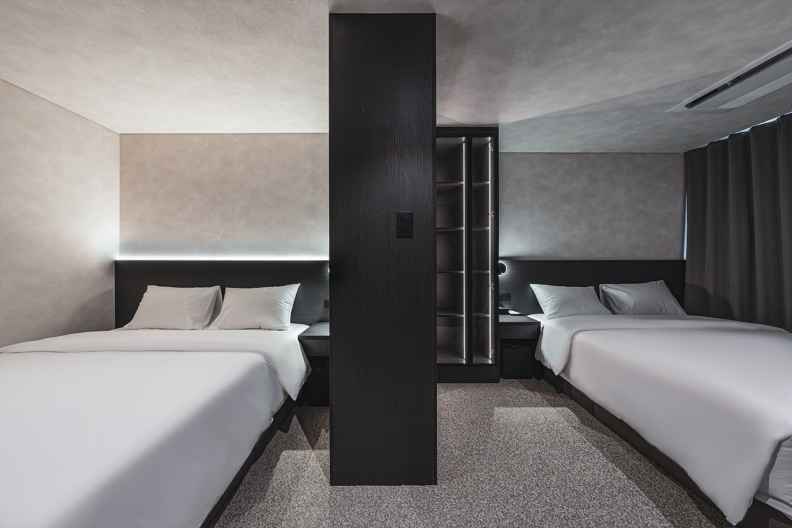 A modern hotel room with two beds, a large dark column, and a built-in wardrobe.
