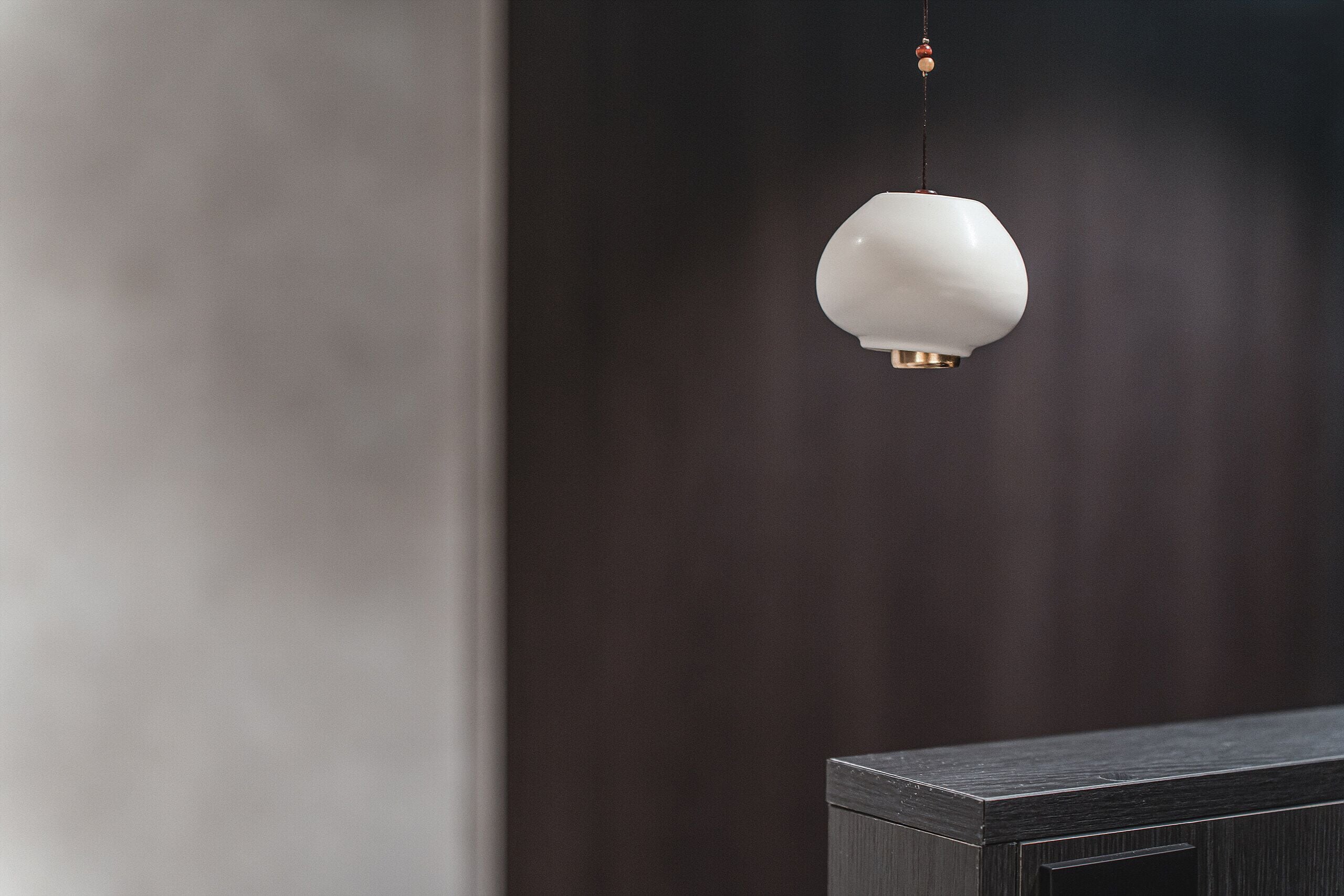 A modern, minimalist room with a dark wooden cabinet and a white pendant light.