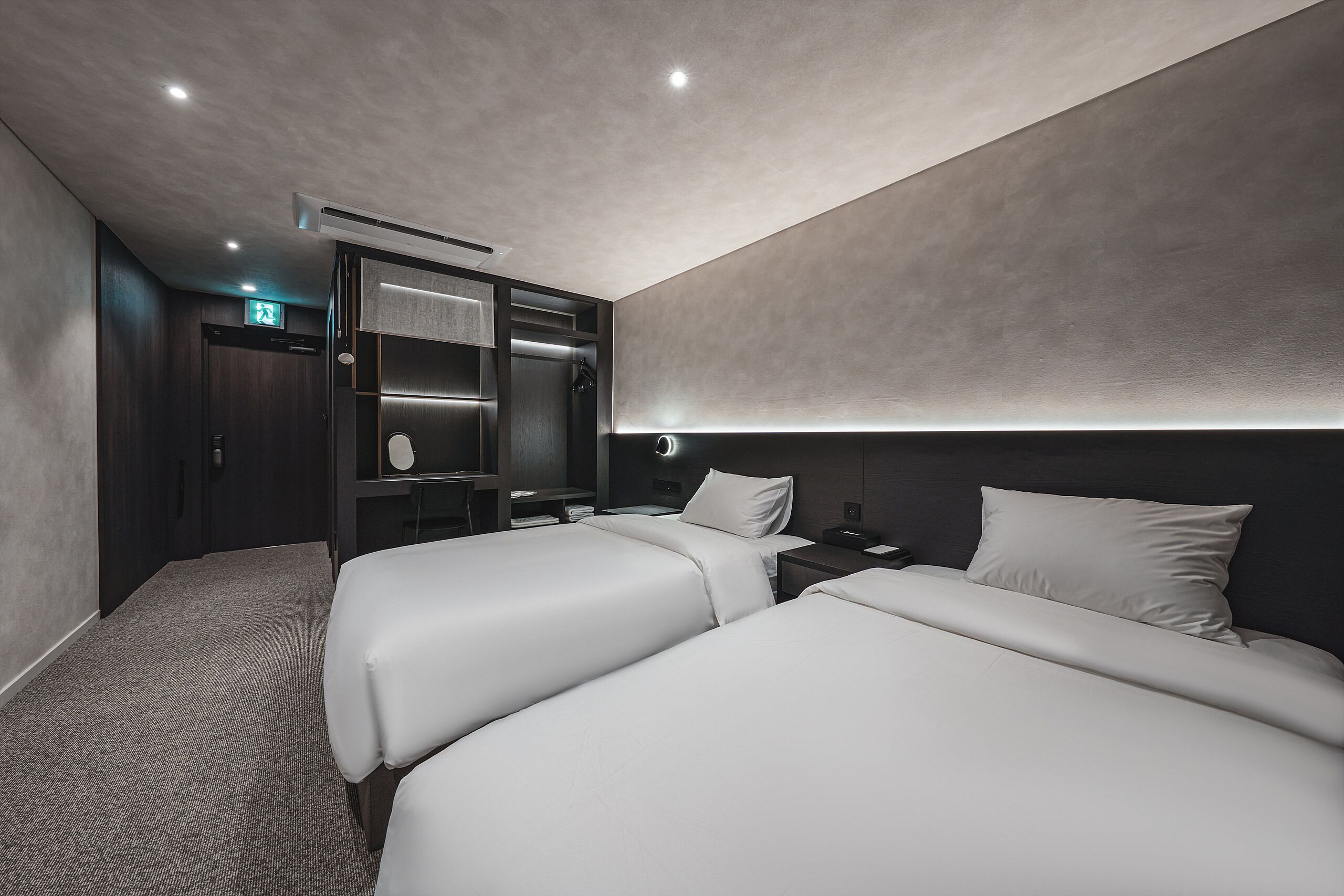 A modern hotel room with two beds, a desk, and a wardrobe.