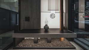 Un espace d’accueil comprenant un comptoir de réception, un vase avec des branches, un panneau fixé au mur et une porte avec une poignée.