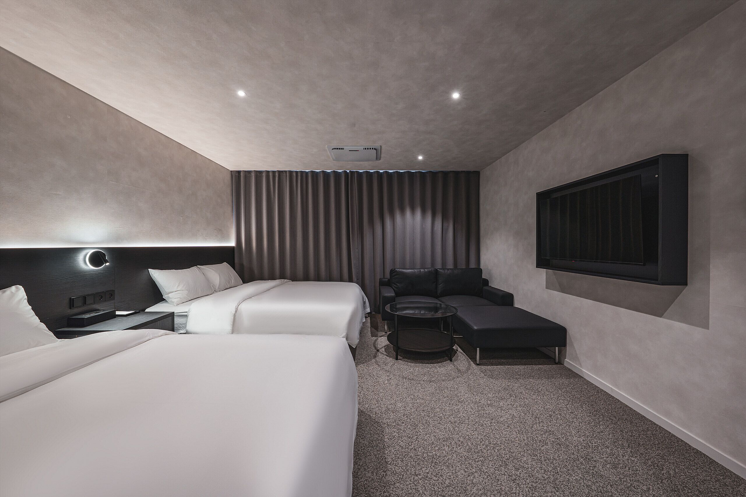 Une chambre d’hôtel moderne avec deux lits, un canapé, une table basse et une grande fenêtre.